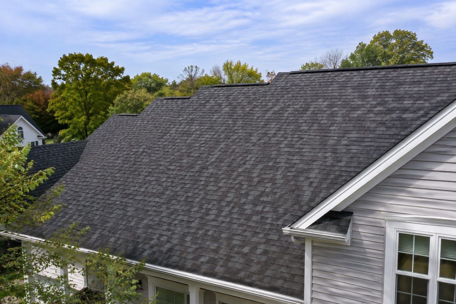 Charcoal shingle roof with white trim and gray siding beneath a soft blue sky.